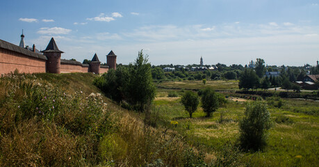 Fototapeta na wymiar Brick walls of the ancient Kremlin in Suzdal russia on a high hill among green trees and grass on a bright sunny summer day and a space for copying