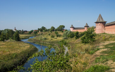 Fototapeta na wymiar Brick walls of the ancient Kremlin in Suzdal russia on a high hill among green trees and grass on a bright sunny summer day and a space for copying