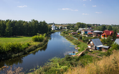 Fototapeta na wymiar Panoramic top view of the city of Suzdal in Russia with historical architecture and a church among the lush green foliage of trees and a small river on a sunny summer day