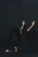 Young woman meditates, doing yoga poses and asana. Fitness girl enjoying yoga indoors. A yoga gymnast girl on a dark background. Black on Black.