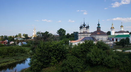 Fototapeta na wymiar Panoramic top view of the city of Suzdal in Russia with historical architecture and a church among the lush green foliage of trees and a small river on a sunny summer day