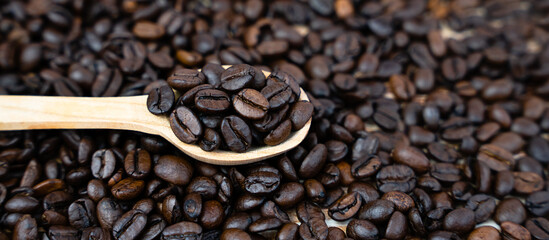 Coffee beans in a wooden spoon on a coffee background. Natural coffee. Banner. Close-up. Selective focus.