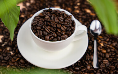 Natural coffee beans in a white cup and spoon on a coffee background. Coffee day. Close-up. Selective focus.