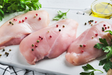 Chicken breast. Two Chicken fillet with spices, olive oil and parsley on white stone cutting board on white wooden table background. Top view with copy space. Food meat cooking background.