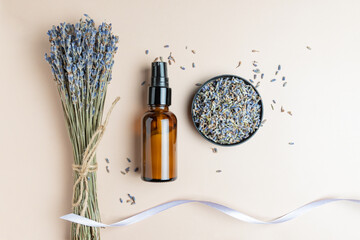 Amber bottle with lavender face cream on beige background. Neutral background with bunch of lavender flowers. Beauty concept for face and body care