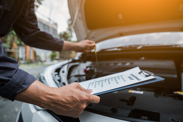 Male mechanic is checking the car maintenance lists for maintenance and fixing the car.
