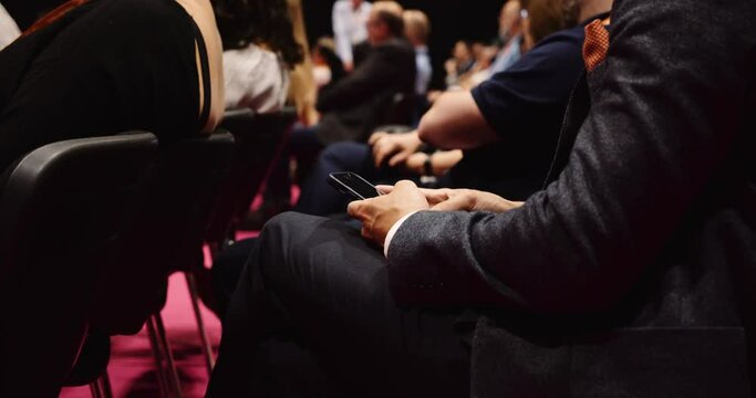 People seated in an auditorium listening to lecture on there cellphone 