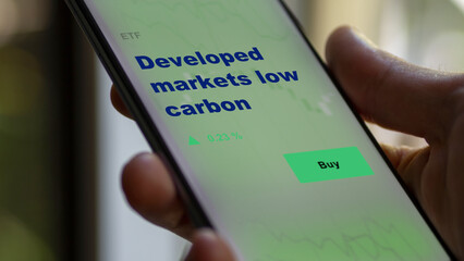An investor's analyzing the green, climate, clean energy etf fund on screen. A phone shows the ETF's prices developed markets low carbon to invest