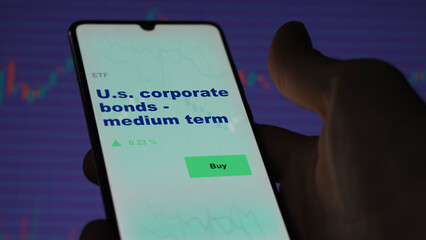 An investor's analyzing the corp bond on screen. A phone shows the ETF's prices u.s. corporate bonds - medium term - obrazy, fototapety, plakaty