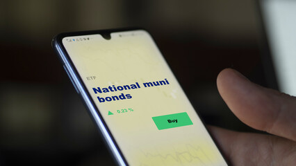 An investor's analyzing the municipal bond on screen. A phone shows the ETF's prices national muni bonds