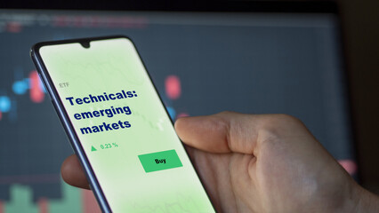 An investor's analyzing the  on screen. A phone shows the ETF's prices technicals: emerging markets
