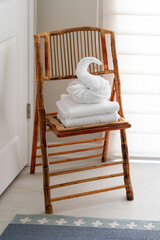 White guest bath towel folded in fancy style in shape of swan sitting atop stack of towels on chair in bed and breakfast hotel bathroom © Christine