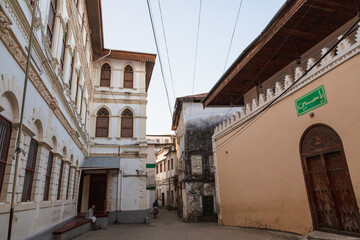 ZANZIBAR, TANZANIA - September 2019: Unrecognizable person sitting on the porch of a white-stone building and a person riding a motorbike in the street in Stone Town