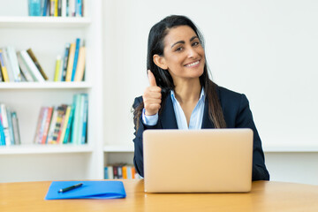 Pretty hispanic mature businesswoman at computer showing thumb up