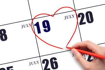 A woman's hand drawing a red heart shape on the calendar date of 19 July. Heart as a symbol of love.