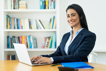 Laughing hispanic mature businesswoman working at computer