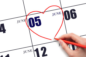 A woman's hand drawing a red heart shape on the calendar date of 5 June. Heart as a symbol of love.
