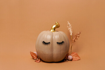 Pumpkin with false eyelashes and autumn leaves on orange background. Autumn, fall, halloween...