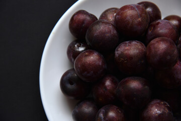 Ripe purple plum fruits on a white plate. Large plum fruits in close-up.
