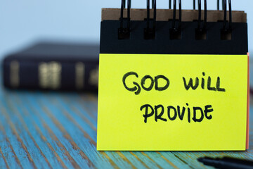 God will provide, a handwritten text note on yellow paper with black marker and a closed Holy Bible...