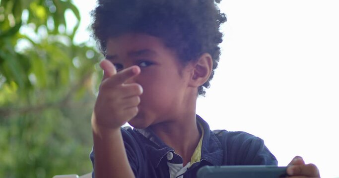close-up, portrait of a child of an African boy who is fooling around looking at the camera, then looking at the phone again
