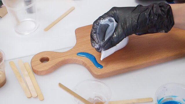 Epoxy resin art. Imitation of the sea. Sea foam. Modern trendy hobby. The pouring process of a wooden. Decorative cutting board. Master carpenter fills a wooden board with epoxy resin. Blue and white