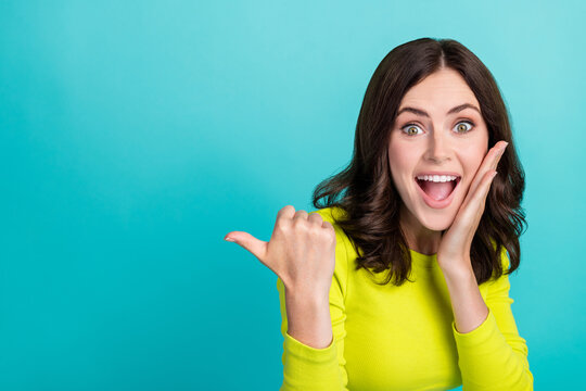 Closeup photo of young attractive girlish woman shocked touch cheeks funny directing finger empty space unexpected isolated on cyan color background