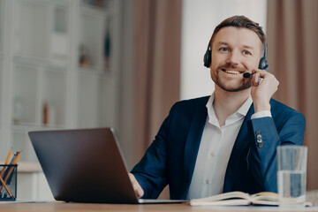 Happy handsome young man using laptop computer with headset