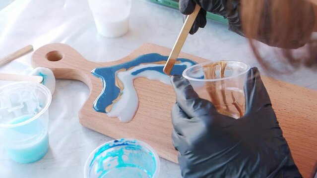 Epoxy resin art. Imitation of the sea. Sea foam. Modern trendy hobby. The pouring process of a wooden. Decorative cutting board. Master carpenter fills a wooden board with epoxy resin. Blue and white