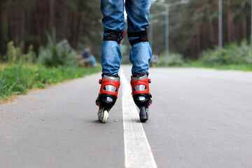 roller skates on the legs of a boy with protection on his knees, riding on the street on asphalt. Rear view