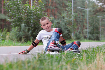 Happy laughing seven years old boy with rollerblades resting sitting on the road in the park on...