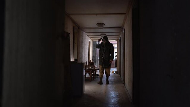 male researcher in a gas mask with a flashlight inside the corridor of an old ruined room, finds canned food in an old refrigerator. The concept of post-apocalyptic world. Looking for food