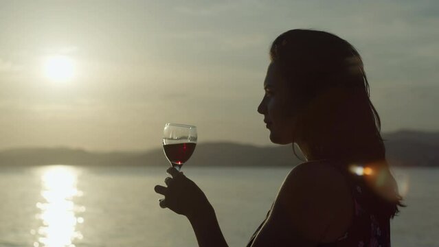 Slow motion video of a girl drinking wine from a glass at sunset by the sea. Lifestyle woman on vacation on the ocean relaxes. High quality 4k footage