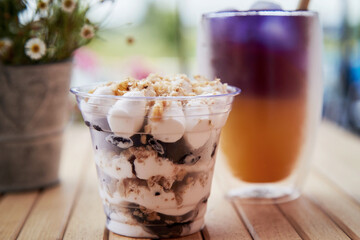  Light natural portion of nuts dessert in a disposable cup. Purple and yellow cocktail with straw reed. Anchan blue tea with antioxidants and nootropics at the terrace near chamomile flowers