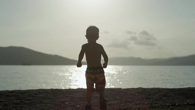 Slow motion video of a baby boy running to the sea. A happy child is looking at the ocean at sunset. High quality 4k footage