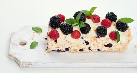 Baked meringue roll with cream and fresh fruits on a white wooden board, delicious dessert