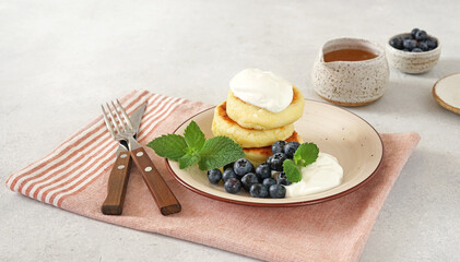 Cottage cheese pancakes, syrniki, curd fritters with fresh blueberries and sour cream on napkin. Side view, copy space for text. Russian breakfast menu