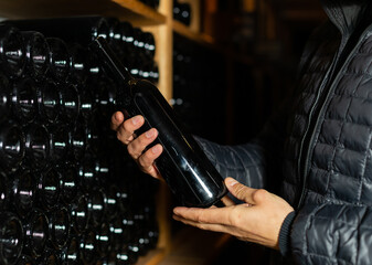 Man in the wine cellar with bottles in background drinking and tasting wine.