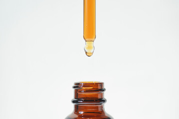 A drop of liquid falling from a pipette into an amber bottle. Skincare products, natural cosmetic on white background. Beauty concept for face and body care.