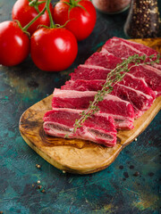 Close-up. Raw meat steaks on a wooden cutting board and red ripe tomatoes on a green background. Cooking homemade meat steaks. Picnic, banquet, family traditions.