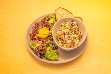A vegan menu plate with a fruit salad and a bowl of white beans with a slice of bread