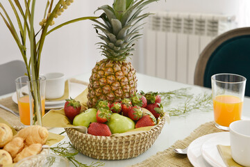 Corner of a kitchen with a white wooden countertop with a wicker basket full of fruit and glasses...