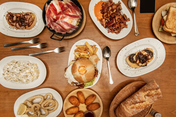 Plates and trays of typical Spanish gastronomy recipes with croquette tapas, grilled ear, alioli potatoes, Andalusian-style squid, toast, sandwich with fried egg, village bread and scrambled ham