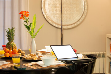 Design dining table in dark wood with breakfast service with fruits and pastries and an open laptop