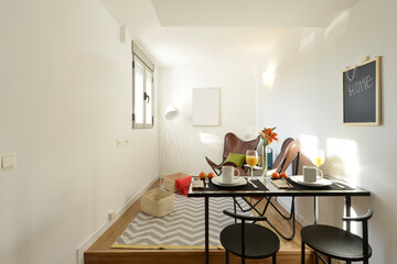 Small room with table for breakfast, orange juice and fruit, leather armchairs, matching black metal chairs and white aluminum window