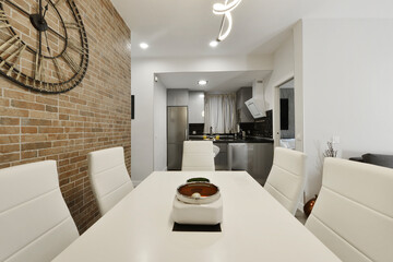 living room with exposed brick wall, white wooden dining table with matching leatherette upholstered chairs and open kitchen in the background