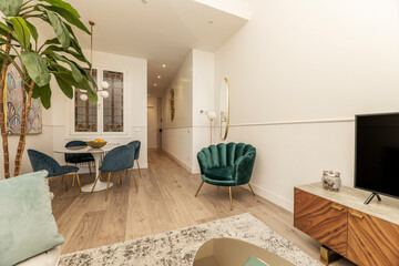 Living room with blue velvet chairs and armchairs, round marble table, fruit bowl and leaded windows, root wood sideboard and decorative indoor plants and oak floor
