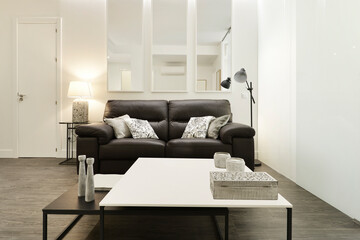 Living room with dark brown leather sofa in lightly decorated room with black and white square wooden side tables