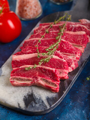 Close-up. Raw meat steaks with a sprig of rosemary, tomatoes on a dark blue background. Recipes for restaurant and home cooking. Banquet, picnic, family holiday, traditions.