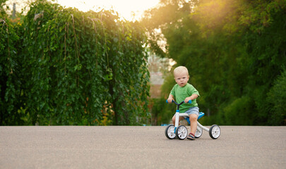Cute little baby boy rides a balance bike in a summer park. Child learning to ride a bicycle